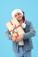 Poster - Happy young man in Santa hat with gift box on blue background