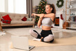 © Pixel-Shot - Sporty young woman with laptop training at home on Christmas eve