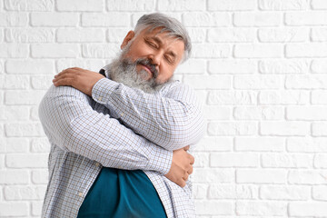 Sticker - Mature man hugging himself on white brick background