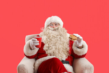 Poster - Santa Claus with cup of tea and tasty burger in armchair on red background