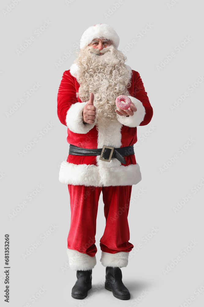 Santa Claus with tasty donut showing thumb-up on white background