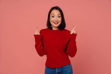 Wall Mural - Smiling woman holding fingers crossed for good luck isolated over pink wall