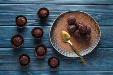 Golden spoon and brigadeiro in plate and on blue wooden background, top view