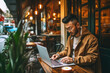 Young Asian man focused on work using laptop in a cozy outdoor cafe