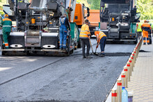 A Team Of Road Workers With Asphalt Pavers Lay Down Fresh Asphalt On A City Street On A Summer Day.