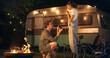 © Kitreel - Young Handsome Man Getting on One Knee to Propose to His Beautiful Girlfriend in a Romantic Atmosphere at a Caravan Rest Area with Campfire and Decorative Lights. Fiance Holding an Engagement Ring.