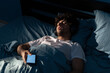 © Andrii Lysenko - Arab man sleeping in bed at night with a smartphone suffers from social media addiction.
