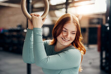 Laughing Young Woman Holding Onto Rings During A Gym Workout