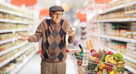 Confused elderly man with a shopping cart holding a receipt at a supermarket