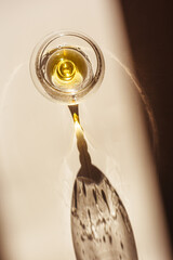 Poster - One glass of cognac sparkling at sunlight, beige background with dark shadow and reflection, sun flare light effect on table. Strong alcohol drink with star filter, top view, desaturated colors