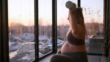 Pregnant Young Woman Doing Fitness With Dumbbells The Sunset On The Balcony	
