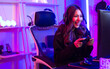 Beautiful happy young female game online streamer or caster smiling with fun, succeed for winner competition, using computer and keyboard to play, sitting in room at home with decorated neon light.