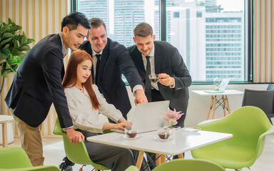 Group of mixed race diverse business people wearing formal clothes, sitting in indoor modern office, using laptop, discussing, brainstorming creative marketing ideas together, smiling with happiness.