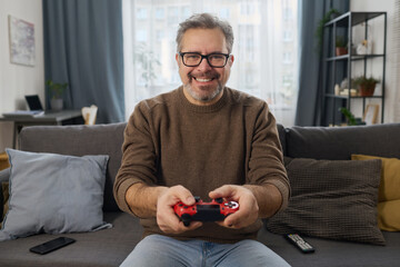 Poster - Portrait of happy man pushing buttons on joystick to play video game on sofa in the room