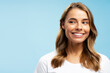 Closeup portrait beautiful smiling young woman with white healthy teeth and stylish wavy hair looking away isolated on blue background, copy space. Health care, dental treatment concept
