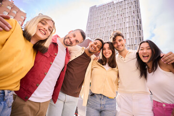 Wall Mural - Portrait large group multiracial friends posing smiling to camera. Happy young people hugging together standing outdoors. Photo of generation z boys and girls enjoying sunny vacation day in the city