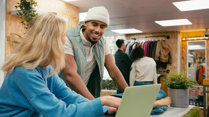 Wall Mural - Male and female sales assistants working at cash desk with laptop in pop up fashion or clothes store with customers in background - shot in slow motion