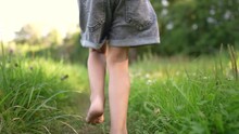 Girl Running On The Grass In The Park In Summer. Happy Family Childhood Dream Concept. A Little Girl With Bare Feet Runs Along The Green Grass In A Summer Park. Child Running Down The Path Lifestyle