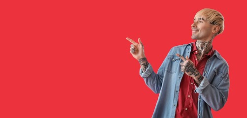 Wall Mural - Tattooed young man pointing at something on red background with space for text
