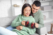 © Pixel-Shot - Happy couple with glasses of warm mulled wine lying on sofa in living room