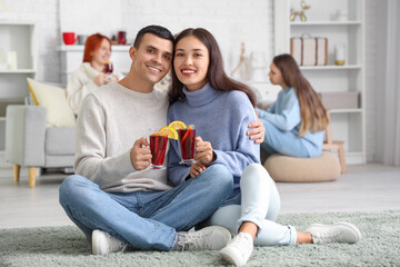 Sticker - Happy couple with glasses of warm mulled wine sitting on floor in living room at party