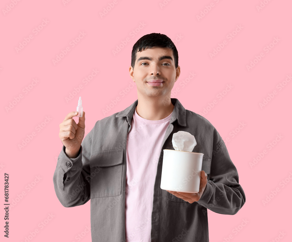 Young man with nasal drops and tissue box on pink background