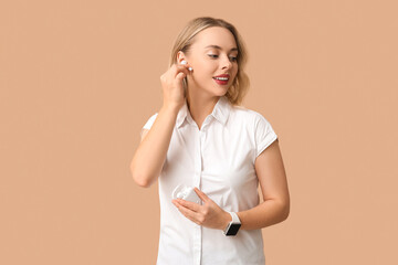 Poster - Pretty young woman with wireless earbuds on beige background