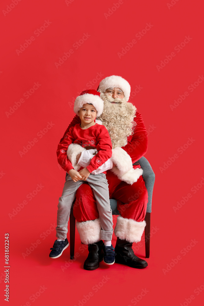 Santa Claus and cute little boy on red background