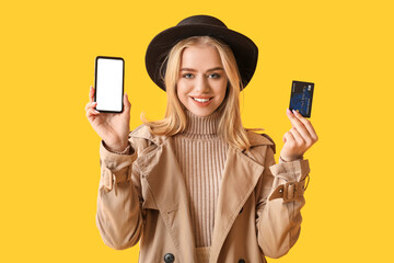 Poster - Young woman with modern mobile phone and credit card on yellow background