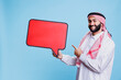 © DC Studio - Smiling muslim man holding red speech bubble mockup and pointing with finger portrait. Person dressed in arab traditional clothes standing with message banner and looking at camera