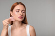 © New Africa - Young woman massaging her face with rose quartz gua sha tool on grey background, space for text
