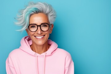 Wall Mural - Portrait of smiling senior woman in pink hoodie and glasses on blue background