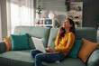 © Zamrznuti tonovi - A woman is talking on the phone while sitting at home and using a laptop.