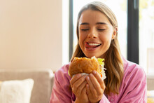 Hungry beautiful woman eating tasty  American burger sitting in cafe