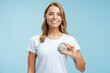 Portrait of attractive woman in white t shirt holding pacemaker in hand, looking at camera isolated on blue background. Female with silky wavy hair standing in studio. Health care, treatment concept