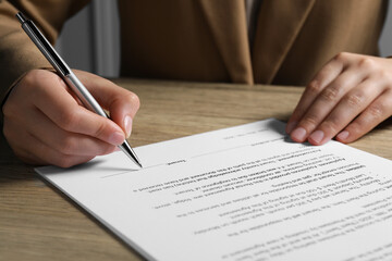 Wall Mural - Woman signing document with pen at wooden table, closeup