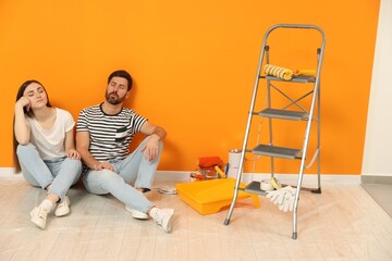 Sticker - Tired designers sitting on floor and painting equipment near freshly painted orange wall