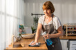 © Kawee - Caucasian senior elderly woman wearing apron, cleaning kitchen at home.