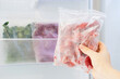Female hand holds plastic bag with a zip fastener with frozen strawberries against the background of an open freezer with other vegetables.