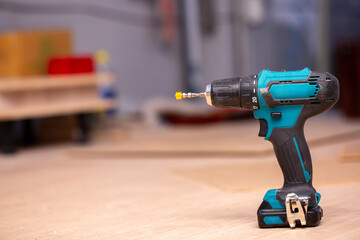 Electric cordless drill driver on the background of a carpentry shop, a professional tool for home repair, a hand power tool, copy space.