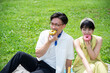 © Monet - Beautiful Asian couple sitting on picnic mats, smiling happily, eating colourful doughnuts.