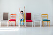 Cheerful little boy and many different colored chairs
