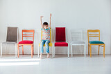Fototapeta  - Cheerful little boy and many different colored chairs