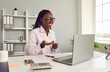 © Studio Romantic - Happy young African American woman business accountant sitting at work desk in office, looking at laptop computer, having online meeting via video call, smiling and explaining something to her client
