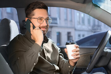 Canvas Print - Coffee to go. Smiling man with paper cup of drink talking on smartphone in car