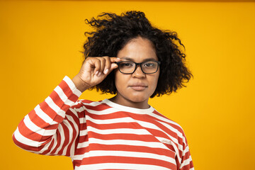 Wall Mural - Curly young woman in glasses on yellow background