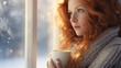 Beautiful model in cozy clothing looking outside the window to a winter scene with a cup of hot coffee
