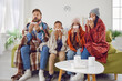 Achoo. Family of four have caught bad cold all together. Sick mom, dad and children in warm clothes and plaids sitting on couch in living room and sneezing in paper handkerchiefs. Winter, flu concept