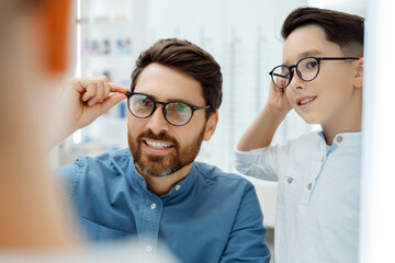 Wall Mural - Smiling man and boy posing in optical store with glasses