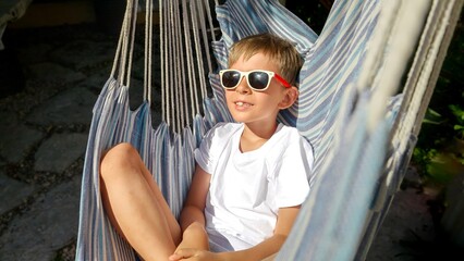 Wall Mural - Carefree childhood and vacation relaxation with this captivating video of a boy in a hat, swaying in a serene garden hammock